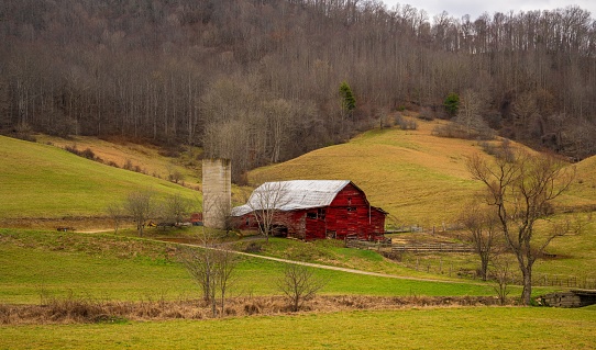 A vibrant red barn is perched atop a lush rolling hill in the countryside of Pennsylvania