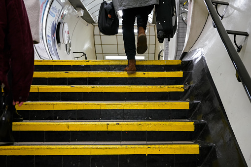 London, United Kingdom - February 02, 2019: Anonymous passengers walking up stairs from underground tube train, view from behind legs and feet visible only