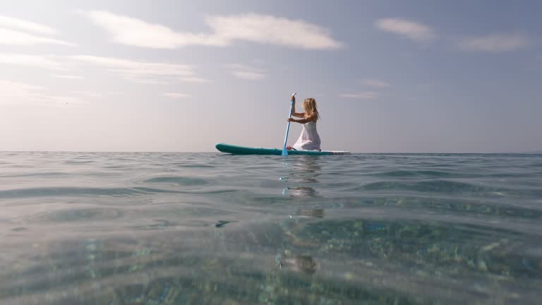 Young woman paddles board in white dress