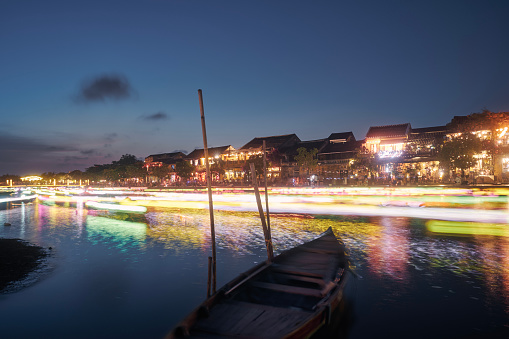 Light trails of boats with traditional lanterns on the motion. Night scene of water canal and waterfront in ancient city Hoi An in Vietnam.