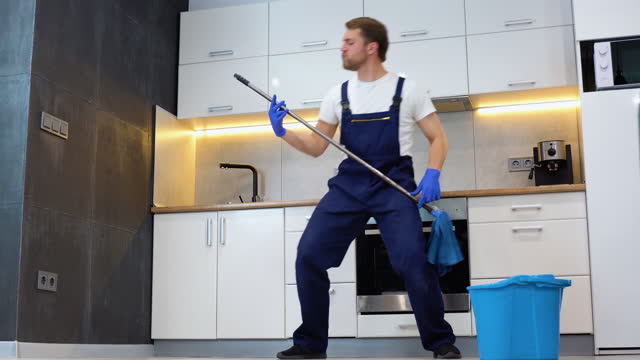 Funny cheerful professional cleaner with mop depicts plays the guitar during a break. Rock star in the kitchen