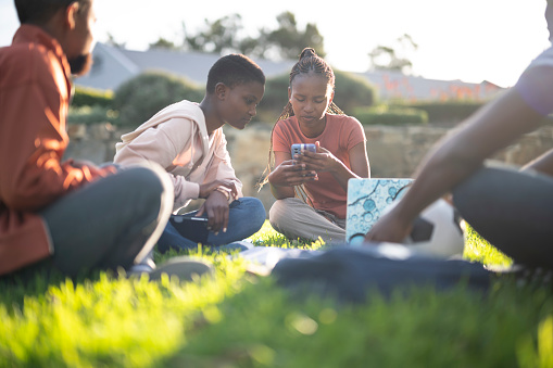 Male & female students in a study group sit together on the lawn & look at notes on the smartphone
