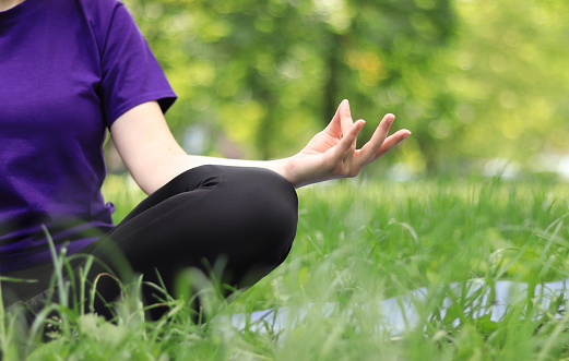 Meditation outdoors in spring or summer. Sports or recreation. A girl sitting in a meditation pose on a yoga mat in the lotus position. Practicing yoga on a sunny day