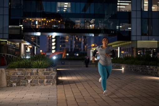 Athletic African woman running alone on the sidewalk in the city at night