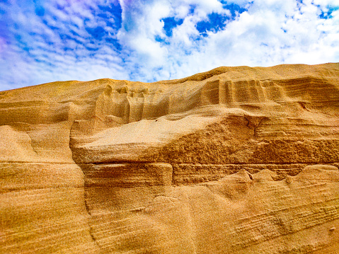 Sand canyon and blue sky with white clouds - photo of a sand dune against a blue sky with white clouds. Small grains of sand. Dune background. The wind blew away the sand. Clouds in the sky. Mountain of sand and the sky.
