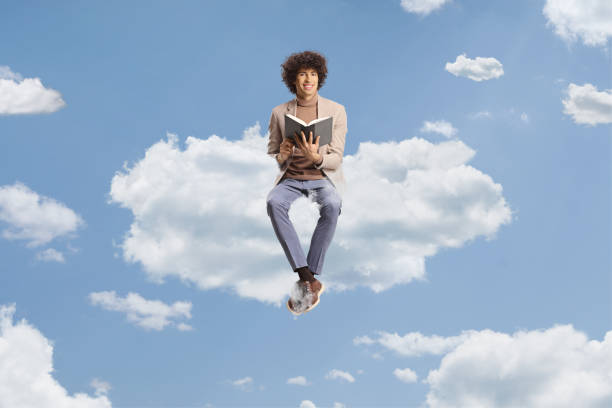 istock Young man with curly hair sitting on a cloud and holding a book 1494831752