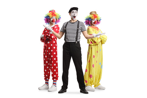 Three boys dressed up in colorful party clothing are celebrating a birthday. One child is wearing a colorful clown wig, a red nose, and a giant bow tie, the other two boys have party hats and funny sunglasses on, one of them is blowing a party blower. This is a tinted, retro style image of the childrens party.