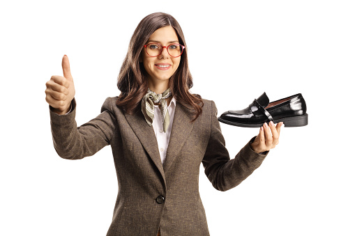 Young woman holding a black loafer shoe and gesturing thumbs up isolated on white background