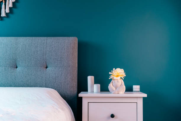 istock Cozy bedroom with turquoise blue walls, white bedside table with ceramic female body-shaped vase with flower and candles. Dark modern stylish female room. Self recovery place at home. Selective focus. 1494832097
