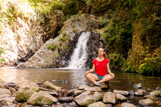 una joven hace yoga y medita cerca de una cascada - waterfall zen like women meditating fotografías e imágenes de stock