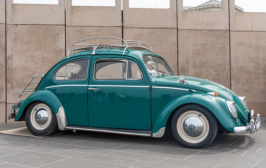 Cenaia, Italy - November 5, 2022: a beautiful Volkswagen Beetle, painted in rich yellow, is parked near a van with the brand colours of Segafredo, an Italian brand of coffee