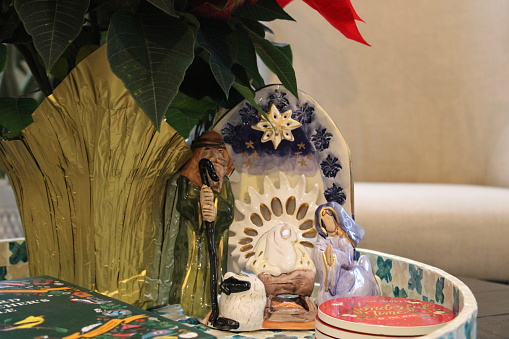 A tray on top of the coffee table that is filled with Christmas decorations, a nativity set, coasters, and a potted poinsettia plant.