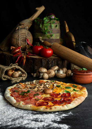 Italian Pizza Four Seasons (Pizza Quattro Stagioni) with different ingredients on the wooden table in the kitchen. Italian homemade recipes