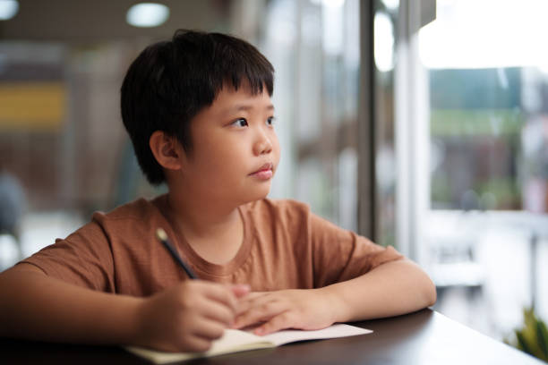 istock A close-up of an Asian boy using a pencil to write and draw on a white book 1494840765