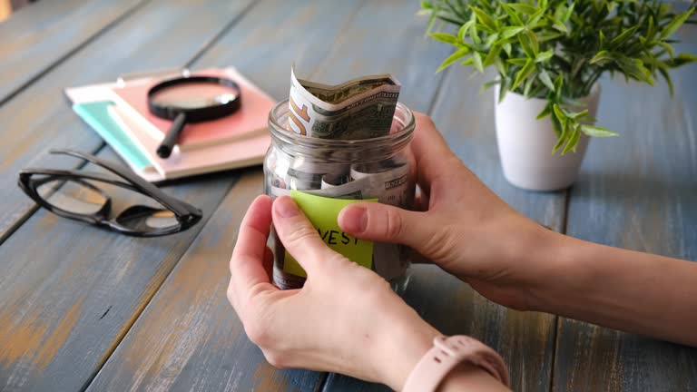 Hands glue a sticker with the text Invest on a glass jar with money, investment concept.