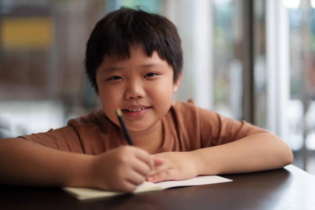 istock A close-up shot captures an Asian boy looking at the camera while using a pencil to write and draw on a white book 1494842399