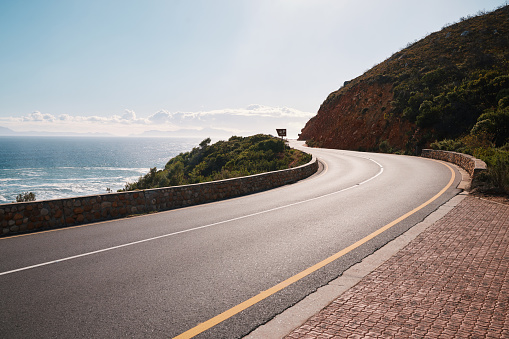 Mountain, road and ocean view with no people for travel, destination or sightseeing in Cape Town. Nature, beauty on empty street for road trip, vacation or holiday on South Africa blue sky background