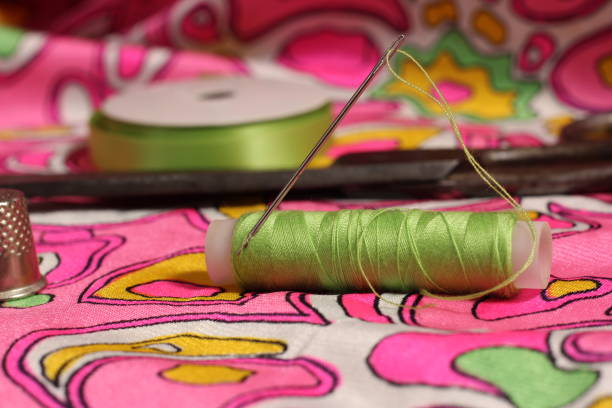 istock Spool of Green Thread, Thimble and Needle on Retro Pink and Green Fabric 1494851131