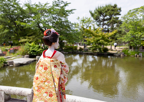 Rear view of Japanese Maiko (Geisha in training) standing on bridge in public park in Gion, Kyoto