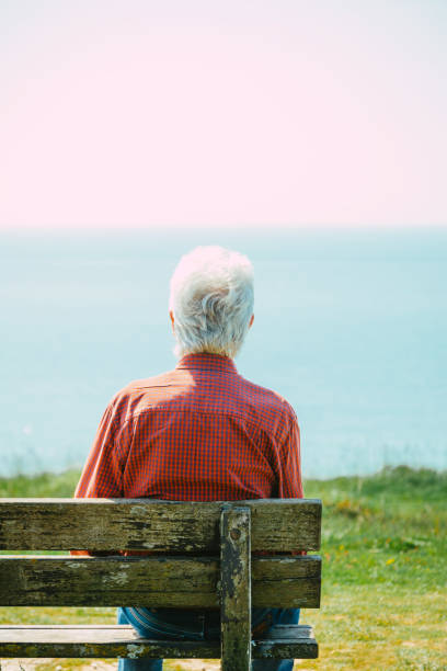 istock Senior man sitting alone on bench looking at sea view 1494853097