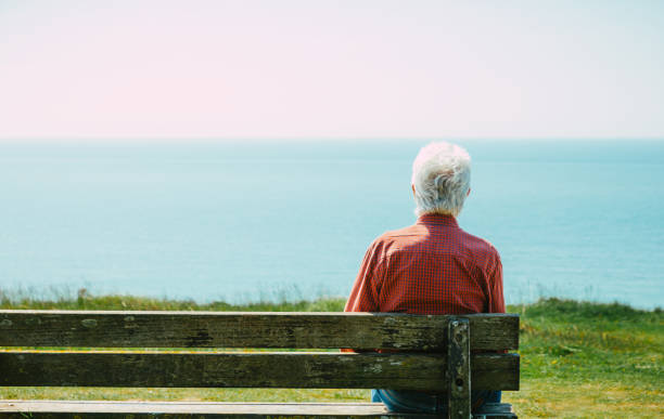 istock Senior man sitting alone on bench looking at sea view 1494853103