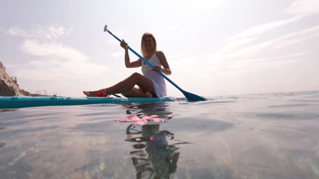 Young woman paddles board in white dress