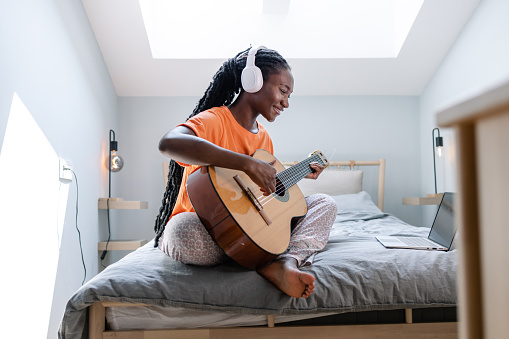 African American woman playing a guitar with the help of online tutorials.