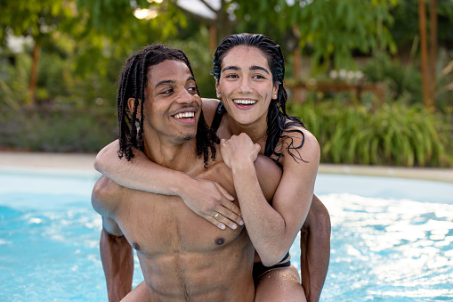 A close up front view of a couple who are enjoying a getaway to Toulouse in the south of France. They are swimming and playing in the pool and the young woman is getting a piggyback from her partner as they swim.