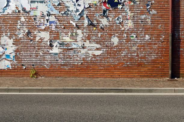 istock Brick wall covered with ripped billboards. Sidewalk and urban street in front. 1494862937