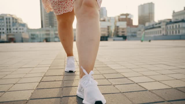View of female legs in white sneakers walking towards the camera.