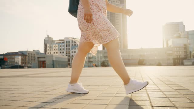 Close up of female legs in stylish white sneakers walking along the city street.