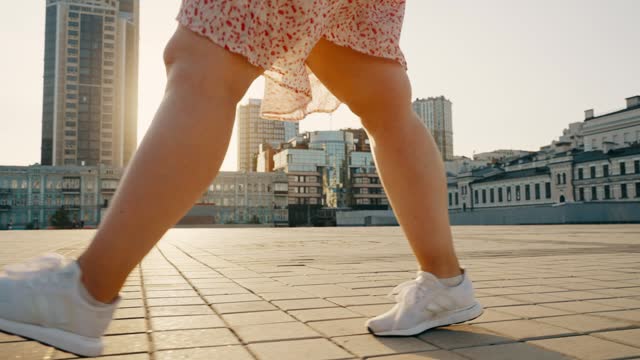 Smooth steps of the legs of a young woman in white sneakers in the sunset rays.