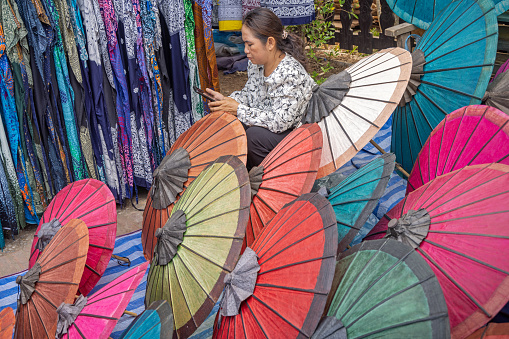 Morning Market, Luang Prabang, Laos - March 21th 2023:  Woman selling umbrellas at the morning market which is the main food distribution site in the former capital of Laos