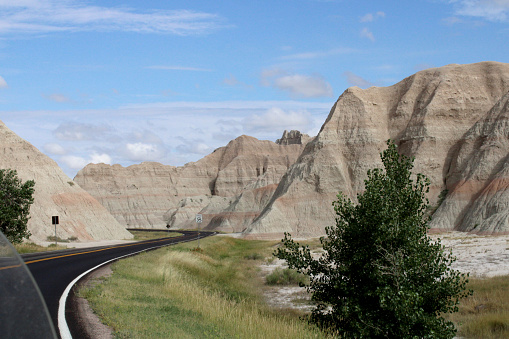 Color landscape photograph of a blacktop road curving through the sandstone rock mountains within the Badlands National Park in South Dakota.