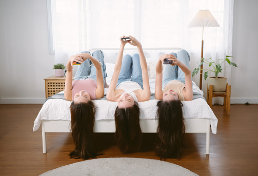 Three young Asian women adorable winsome lovely attractive cheerful happy face lying on bed and texting with her smartphone. Korean girls is social media and chatting. Lifestyle, Friendship concept