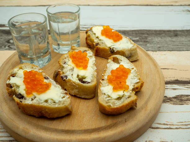 木の皿に赤い魚の卵とヴォクダのグラスを添えたパンのミニスライス - caviar salmon red gourmet ストックフォトと画像