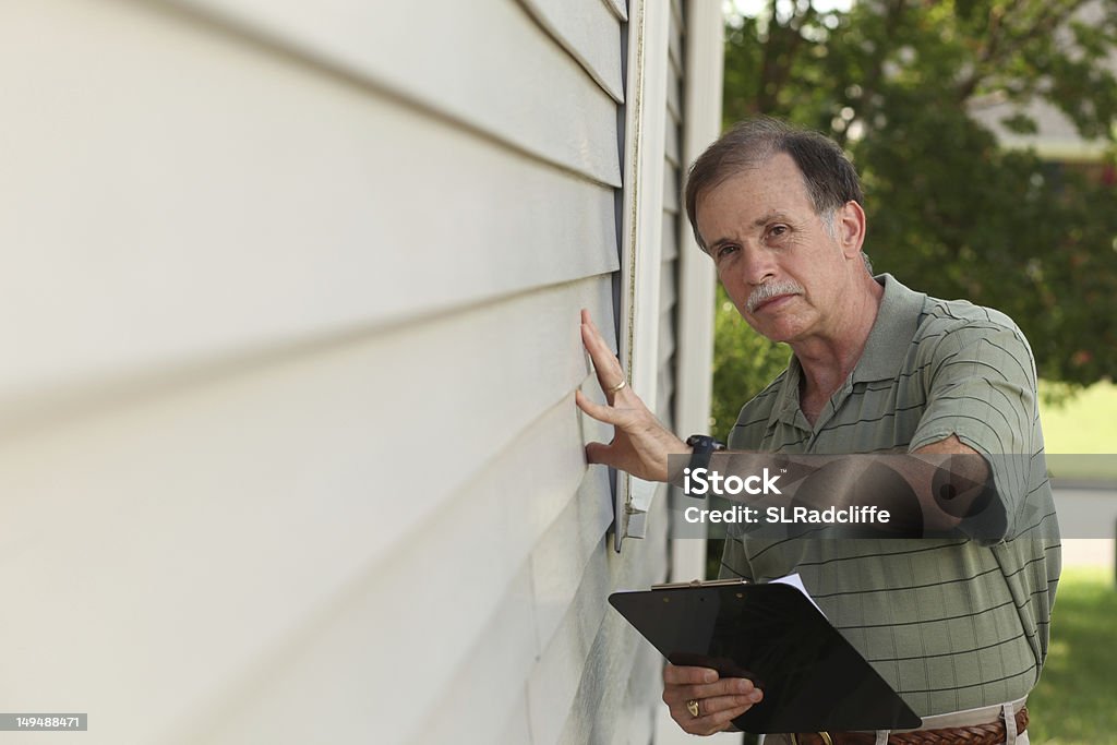 Adult male with clipboard inspects vinyl siding on residential home An adult male inspects residential vinyl siding. Siding - Building Feature Stock Photo