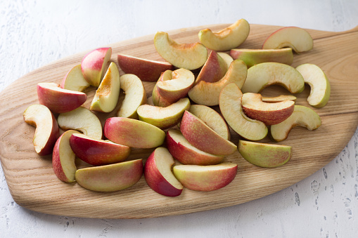 Wooden board with sliced apples for baking or other dishes on a light blue background