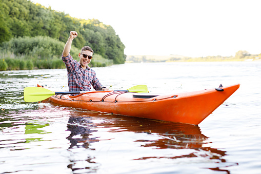 Kayaking on the river. Adult caucasian man is sitting in a kayak and greetings. The concept of the water activities.