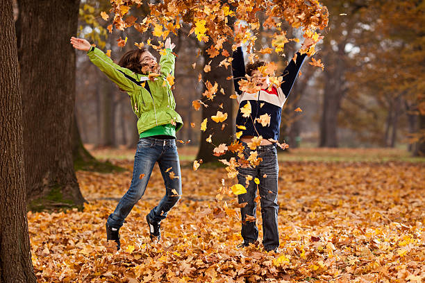 Girl and boy throwing up leaves in park