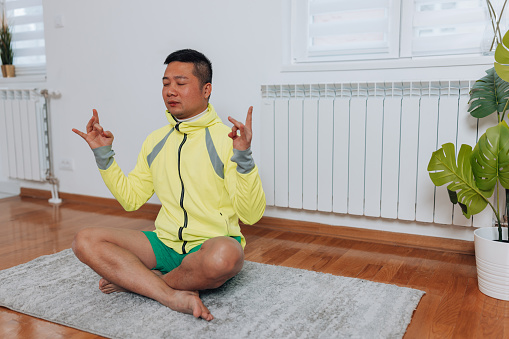 In his sacred space at home, a mid adult Chinese man seeks moments of tranquility and peace, immersing himself in a meditative practice on his exercise mat to find clarity and serenity