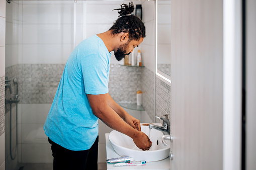 A mid adult African American man demonstrates his commitment to hygiene as he carefully washes his hands in the bathroom sink