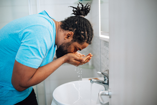 Demonstrating his commitment to skin health, a mid adult African American man takes a moment to nurture his facial skin in the bathroom