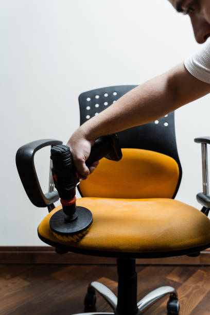 istock Smearing detergent on armchair using drill with brush for dry cleaning. Applying detergent on chair in home interior for dry cleaning. 1494903780