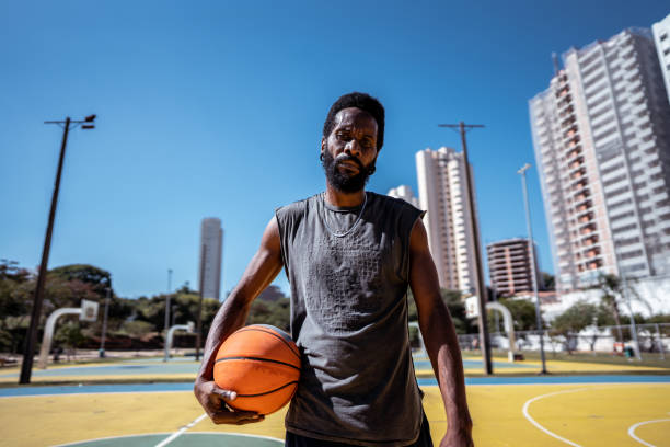 Portrait of a mature man holding a basketball on a sport court Portrait of a mature man holding a basketball on a sport court touch of the sun stock pictures, royalty-free photos & images