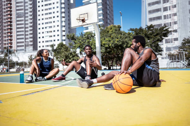 Friends talking while be sitting on ground after play basketball on a sport court