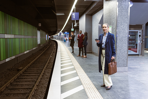 Businesswoman waiting a train in a subway platform. She is using mobile phone. Frankfurt, Germany