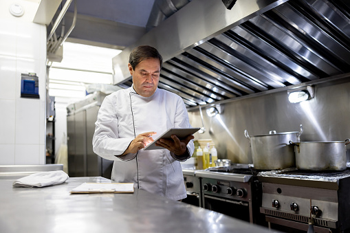 Chef working at a restaurant and creating a menu using a tablet computer and a notepad â commercial kitchen concepts
