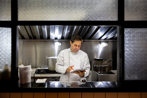 Latin American chef working at a restaurant and looking at a recipe on a tablet computer â commercial kitchen concepts