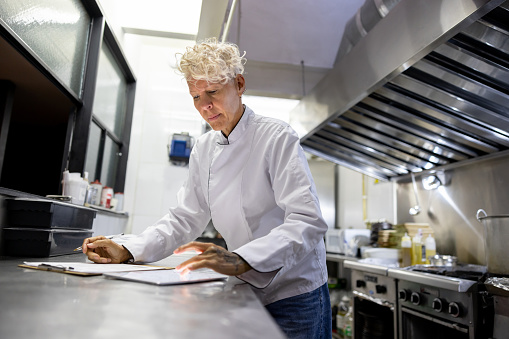 Chef working at a restaurant and creating a menu using a tablet computer and a notepad â commercial kitchen concepts